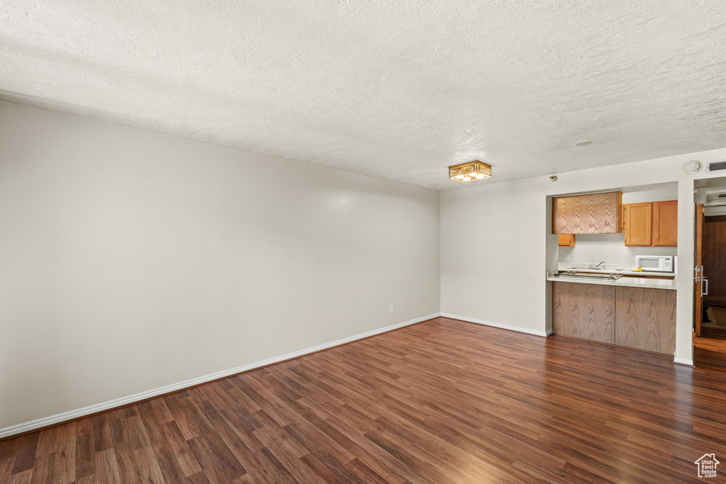 Unfurnished living room featuring dark wood-style flooring, a textured ceiling, and baseboards