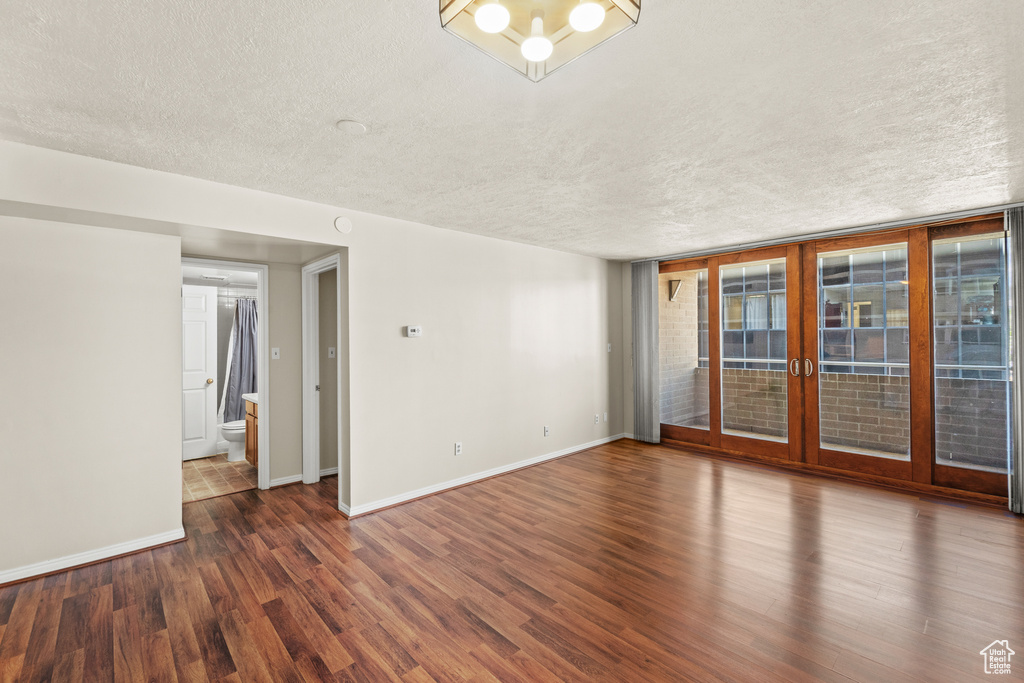 Unfurnished room featuring a textured ceiling, baseboards, wood finished floors, and french doors