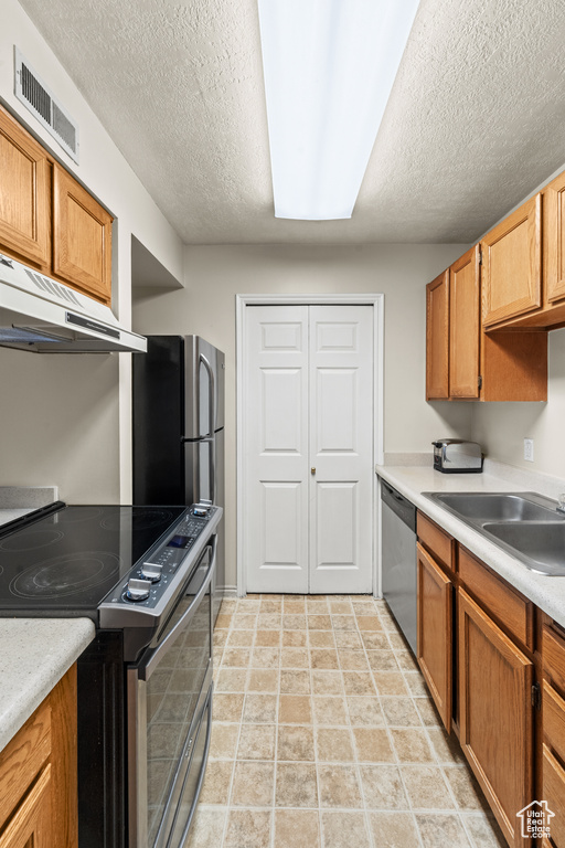 Kitchen featuring stainless steel appliances, under cabinet range hood, a sink, a textured ceiling, and light countertops
