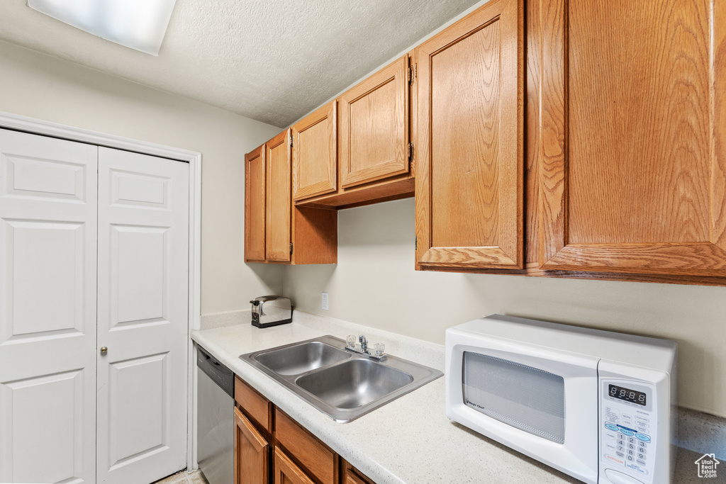 Kitchen with white microwave, a sink, dishwasher, light countertops, and a textured ceiling