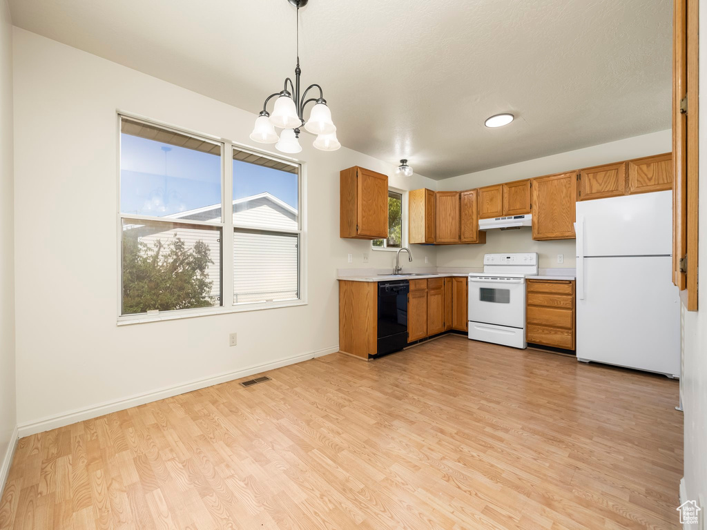 Kitchen with white appliances, under cabinet range hood, light countertops, a sink, and light wood-style flooring