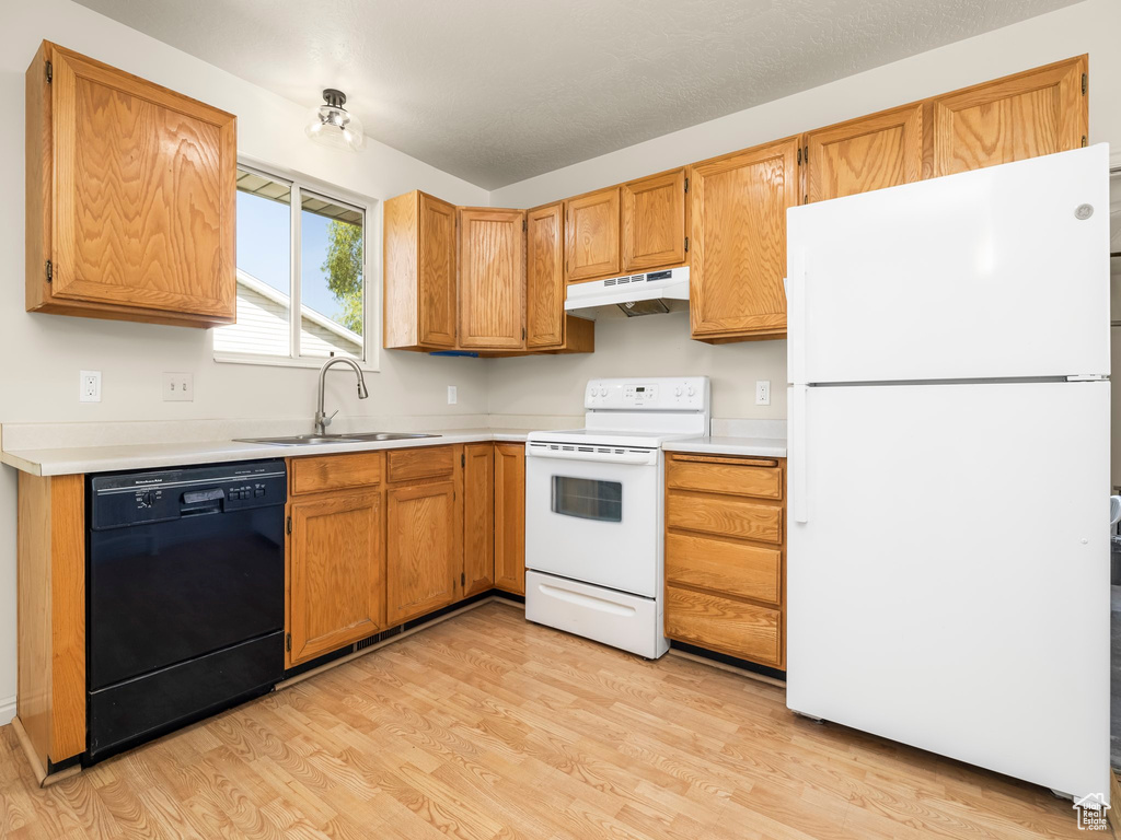 Kitchen with white appliances, under cabinet range hood, a sink, light wood-type flooring, and light countertops