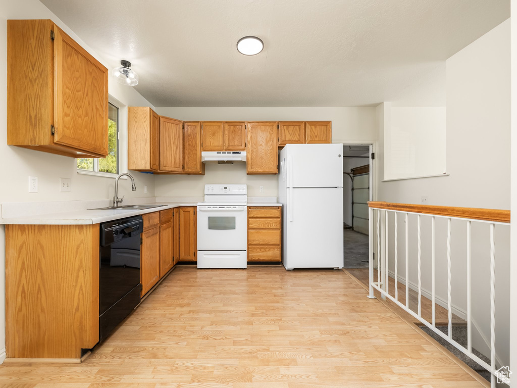 Kitchen with white appliances, under cabinet range hood, a sink, light wood-style floors, and light countertops