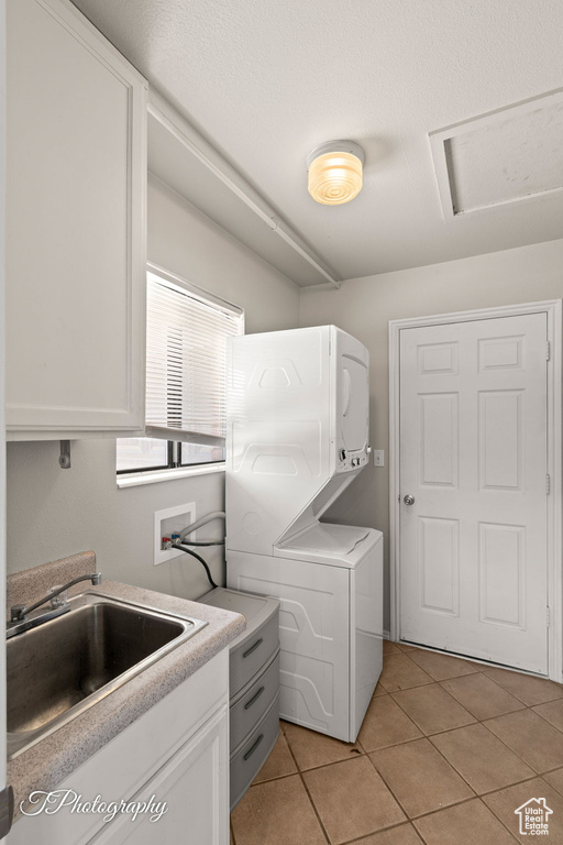 Laundry room with stacked washing machine and dryer, light tile patterned floors, and attic access