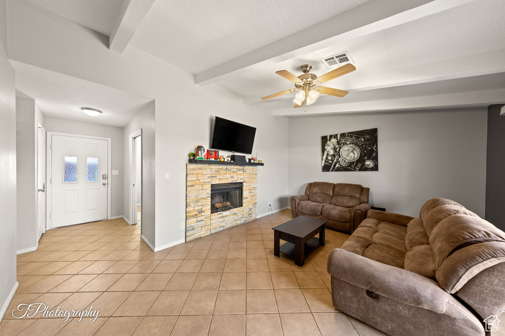 Living area with light tile patterned floors, beam ceiling, ceiling fan, a fireplace, and baseboards