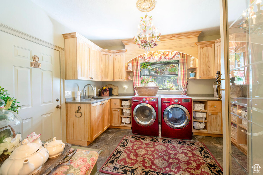 Clothes washing area featuring a sink, washing machine and dryer, cabinet space, and a chandelier