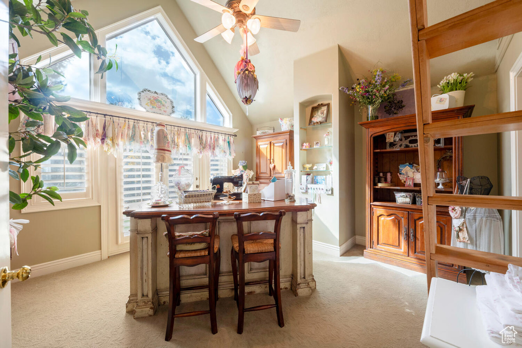 Dining room with baseboards, high vaulted ceiling, ceiling fan, and light colored carpet