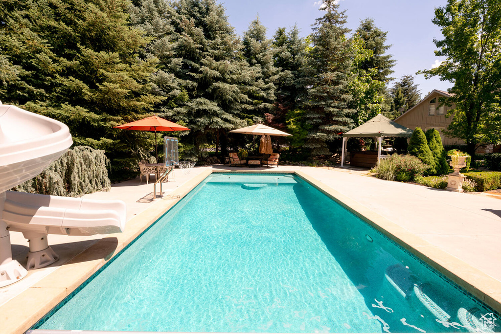 Outdoor pool with a water slide, a patio area, and a gazebo