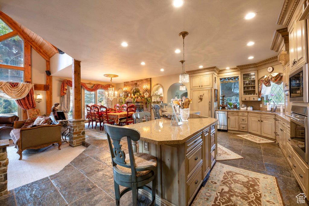 Kitchen with arched walkways, cream cabinets, appliances with stainless steel finishes, a kitchen bar, and stone tile flooring