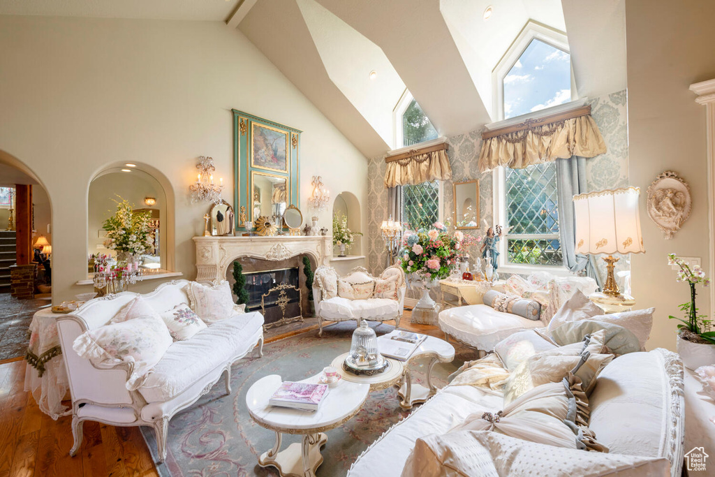 Living area with arched walkways, high vaulted ceiling, a premium fireplace, and wood finished floors