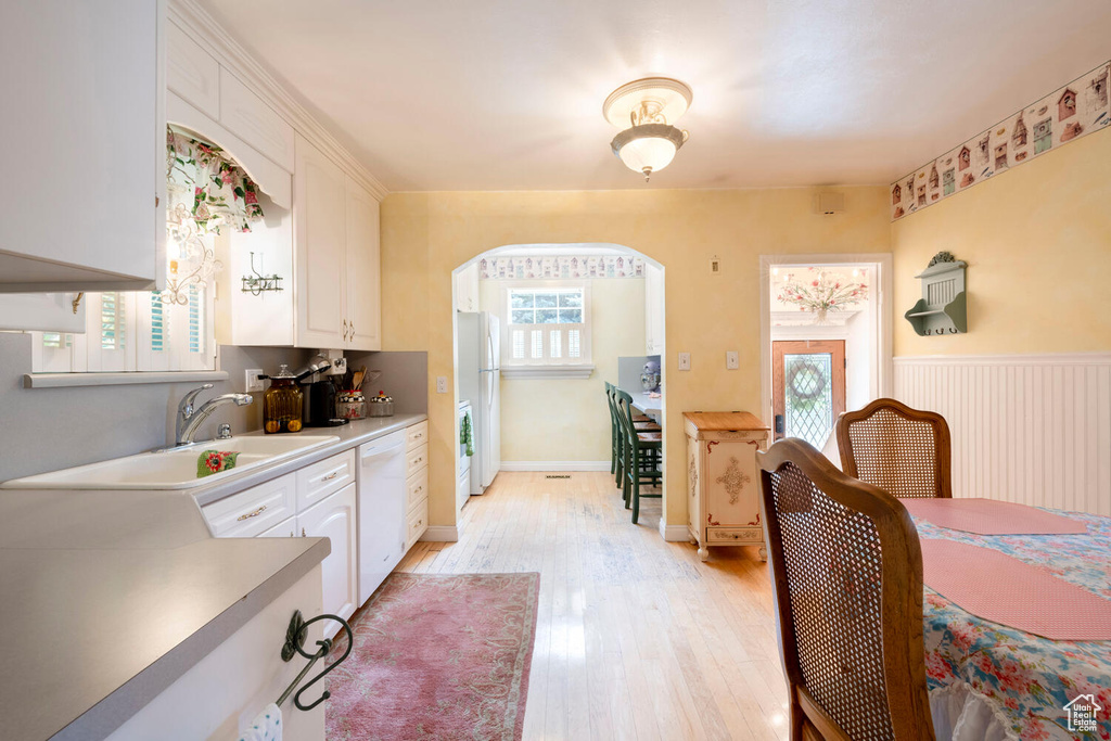 Dining room featuring arched walkways, light wood finished floors, a wainscoted wall, and a healthy amount of sunlight