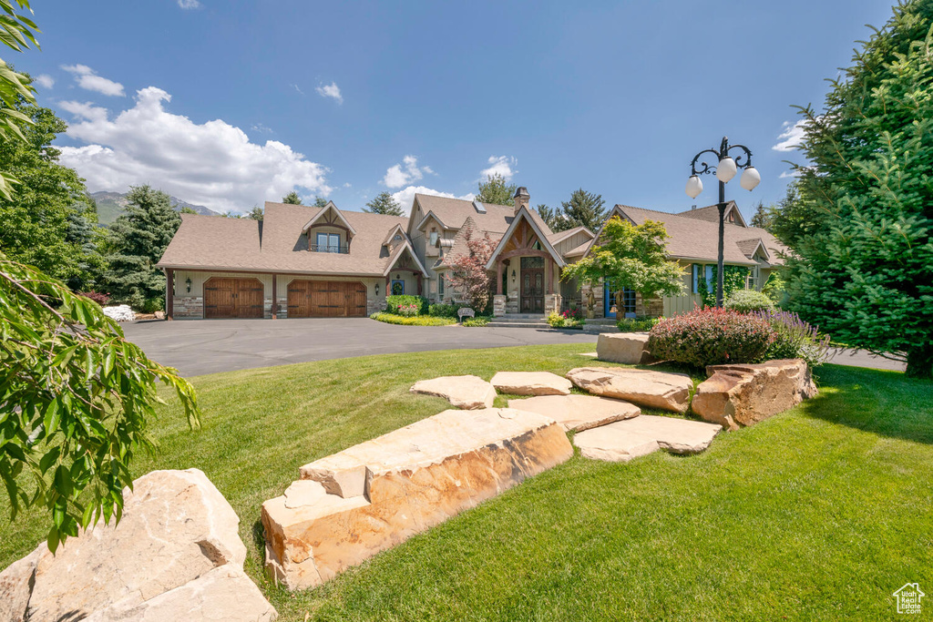 View of front of property featuring a garage, stone siding, and a front lawn
