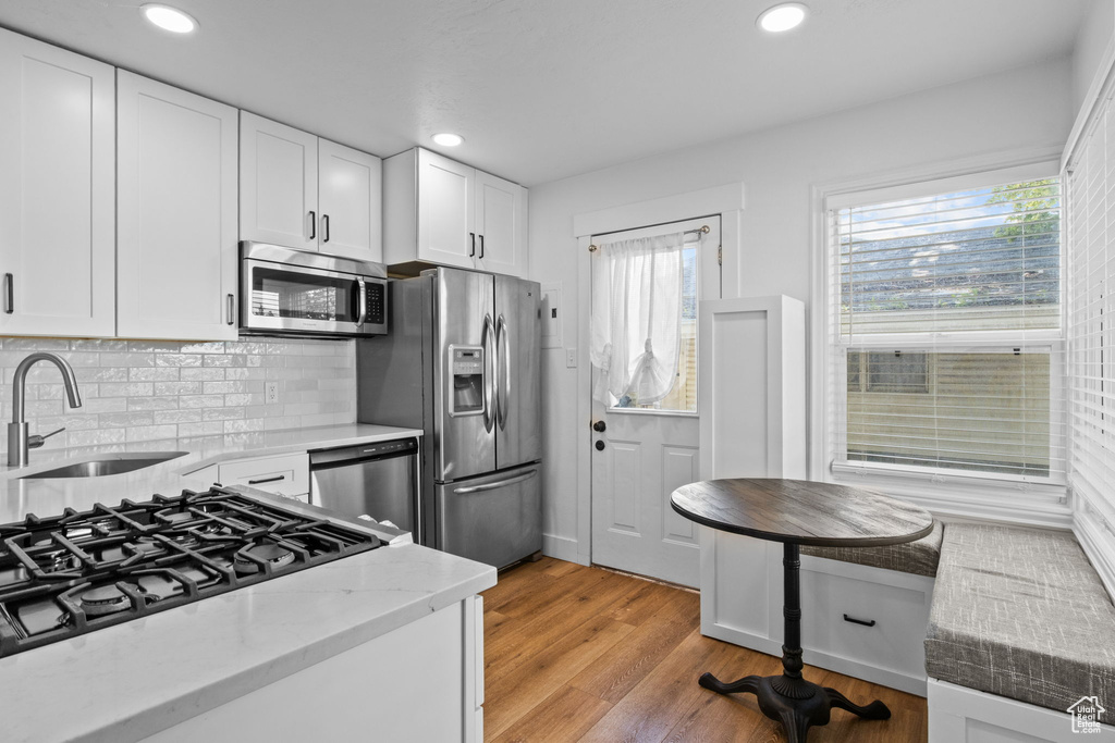 Kitchen with stainless steel appliances, a sink, white cabinets, light wood-style floors, and light stone countertops