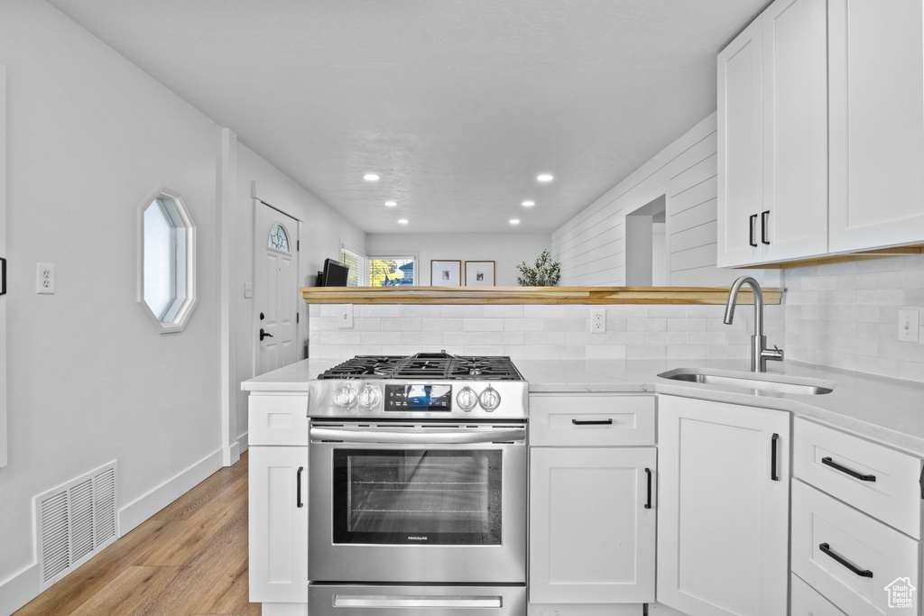 Kitchen featuring stainless steel gas stove, a sink, tasteful backsplash, light countertops, and recessed lighting