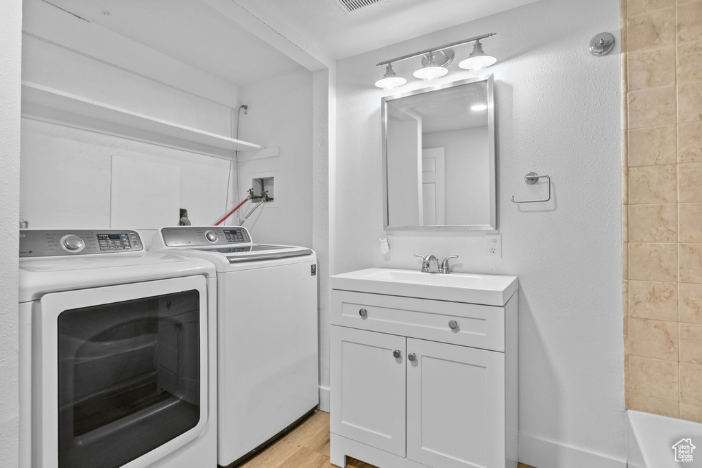 Laundry area featuring washer and clothes dryer, a sink, and light wood finished floors