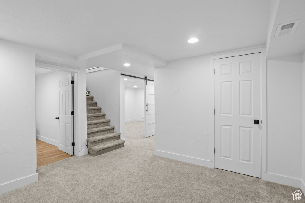 Finished basement with a barn door, carpet flooring, recessed lighting, stairway, and baseboards