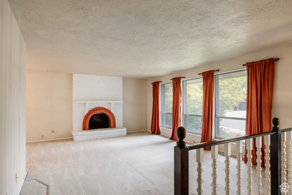 Unfurnished living room featuring a textured ceiling, carpet floors, baseboards, and a fireplace