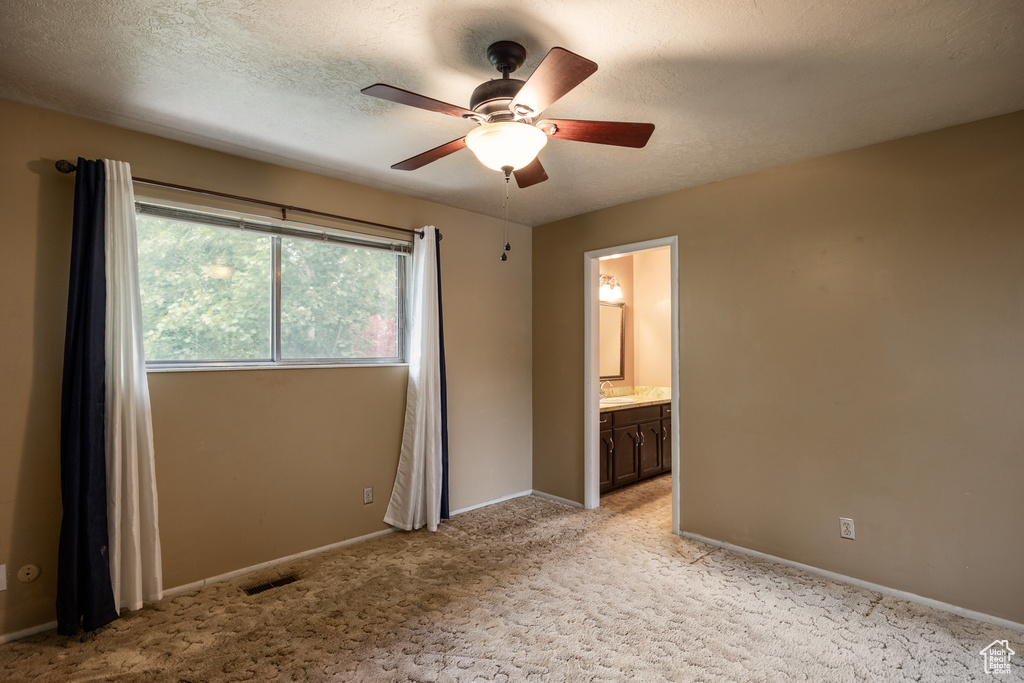Unfurnished bedroom with baseboards, light carpet, a textured ceiling, connected bathroom, and a ceiling fan