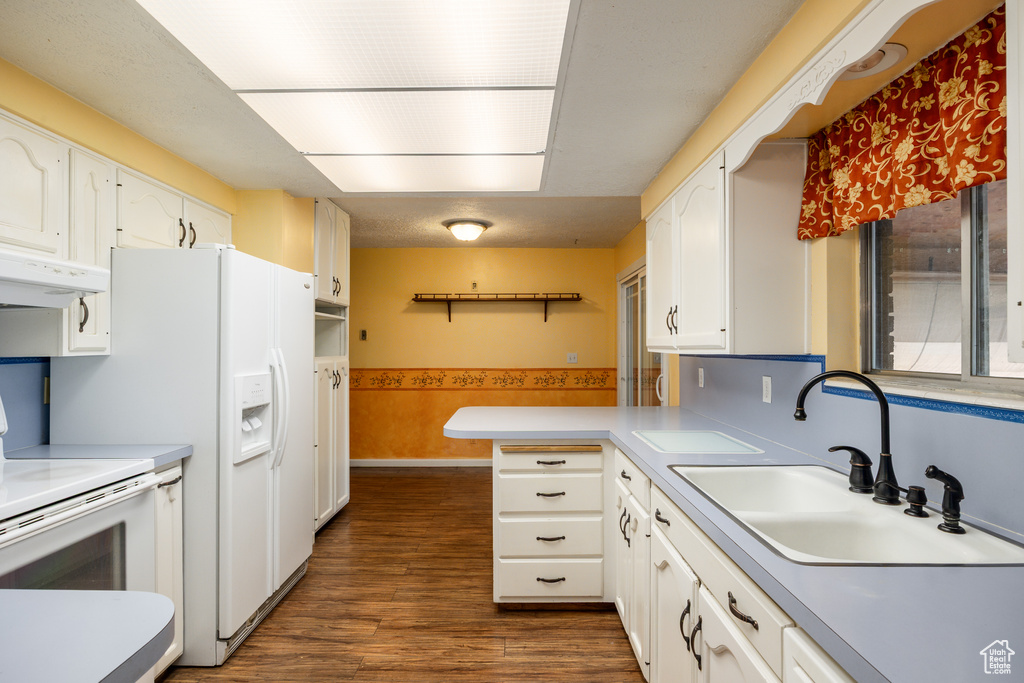 Kitchen with under cabinet range hood, a sink, white cabinetry, a peninsula, and a wainscoted wall