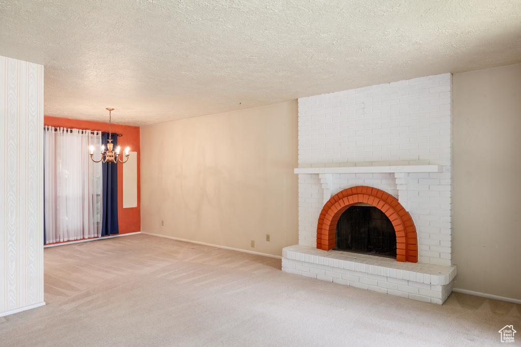 Unfurnished living room featuring a chandelier, carpet, a textured ceiling, baseboards, and a fireplace