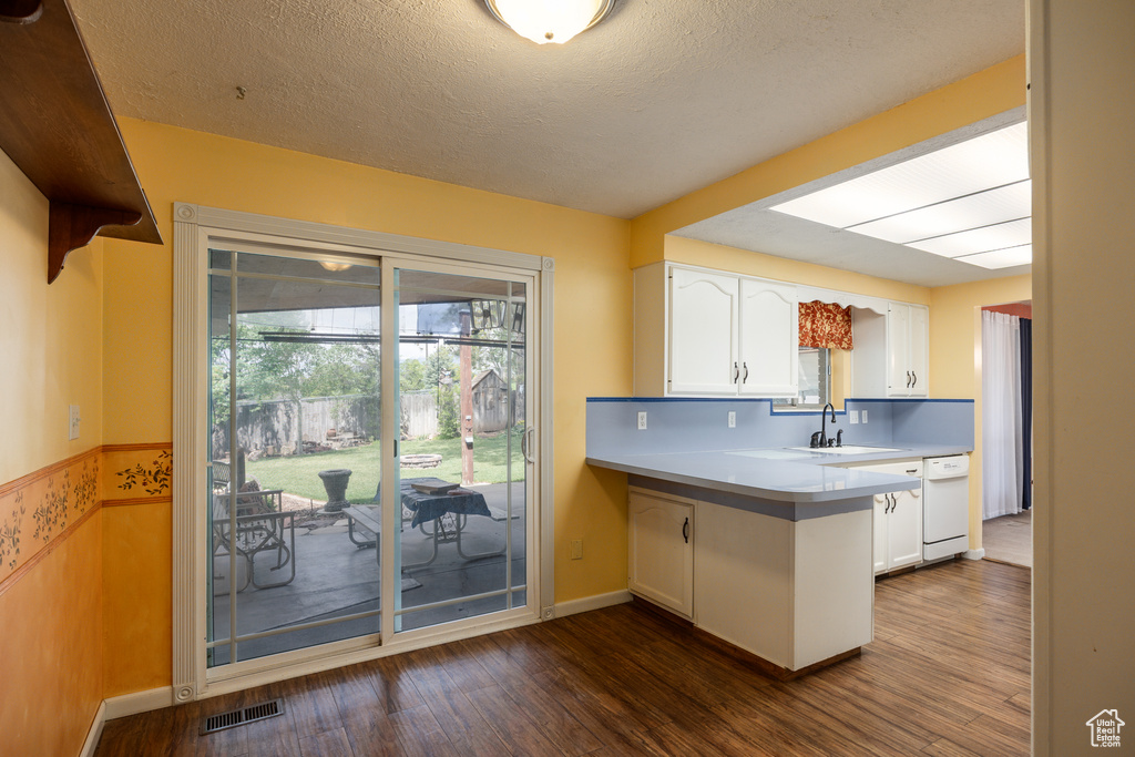 Kitchen featuring white cabinets, a sink, dark wood-type flooring, a peninsula, and a textured ceiling
