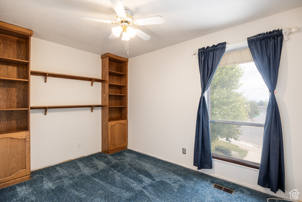 Empty room featuring dark colored carpet and ceiling fan