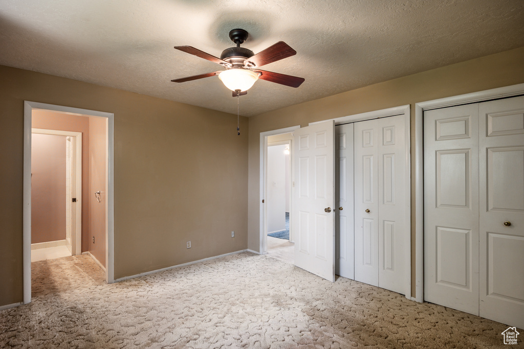 Unfurnished bedroom featuring light colored carpet, multiple closets, baseboards, and ceiling fan