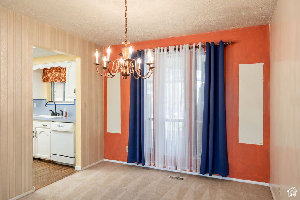 Unfurnished dining area with a chandelier, a sink, a textured ceiling, baseboards, and light carpet