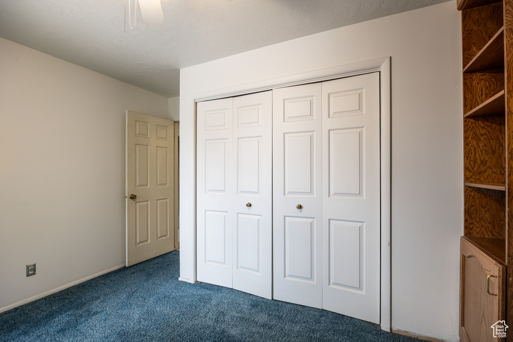 Unfurnished bedroom with dark carpet, a closet, ceiling fan, and baseboards