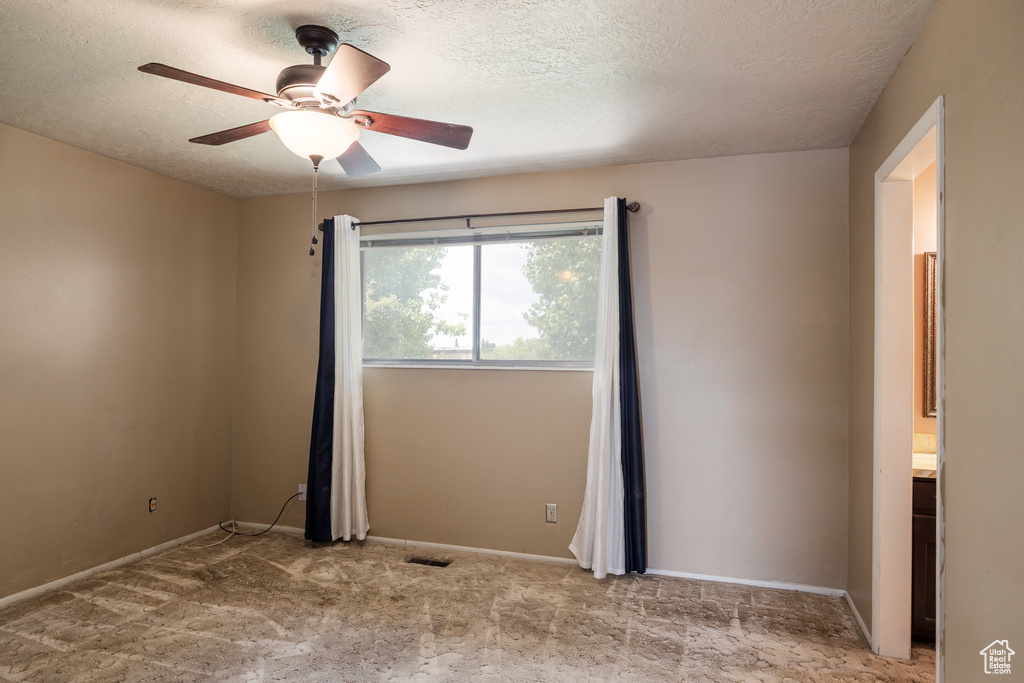 Empty room with a textured ceiling, a ceiling fan, carpet, and baseboards