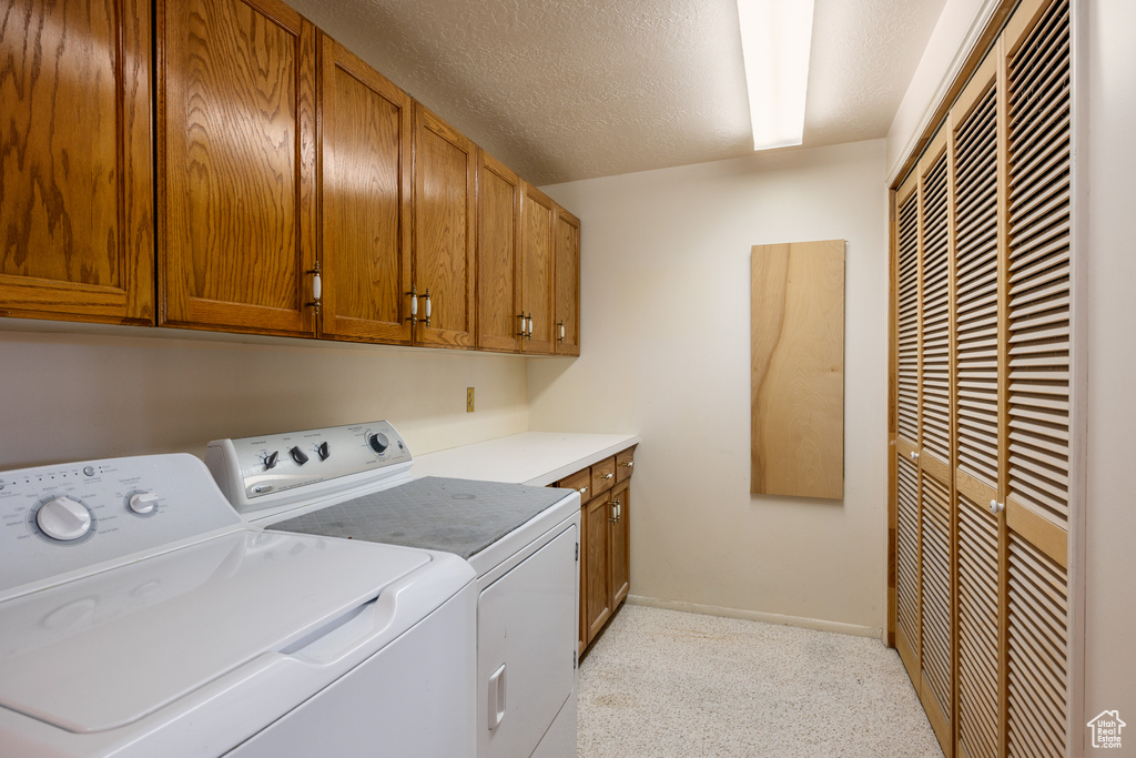 Laundry area featuring independent washer and dryer, a heating unit, cabinet space, baseboards, and a textured ceiling