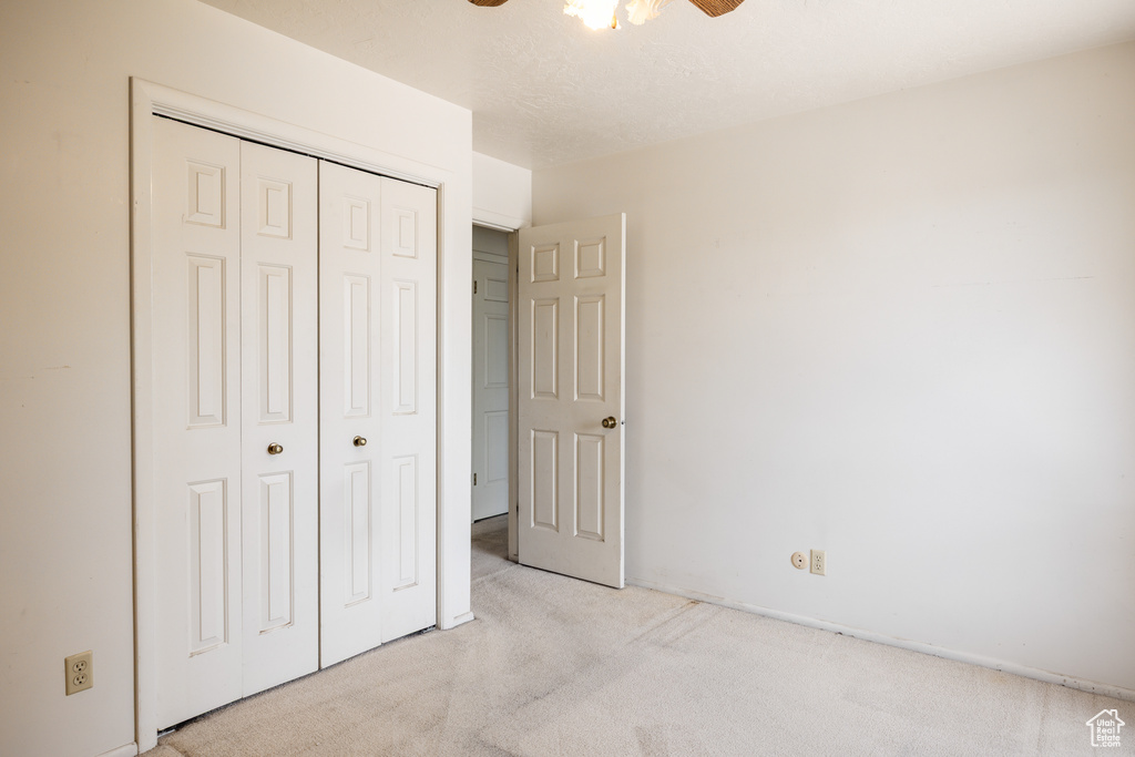 Unfurnished bedroom featuring light colored carpet, a closet, and a ceiling fan