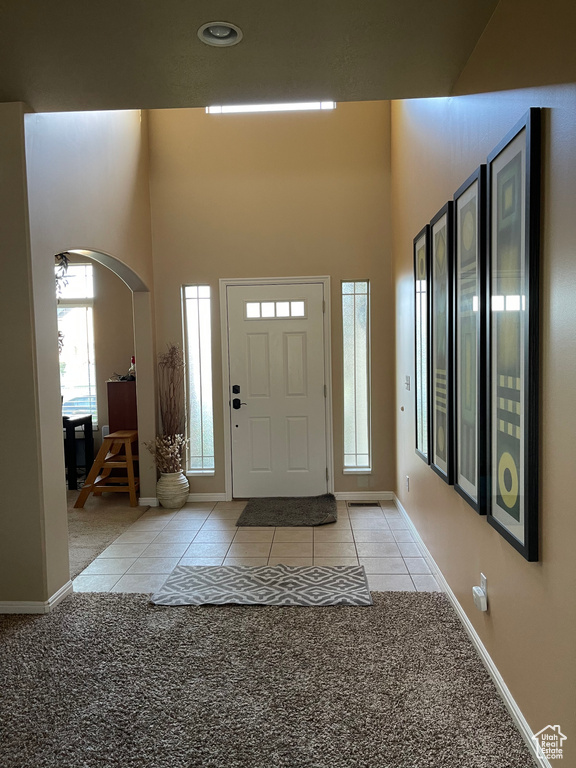 Foyer featuring arched walkways, baseboards, light tile patterned floors, a high ceiling, and light carpet