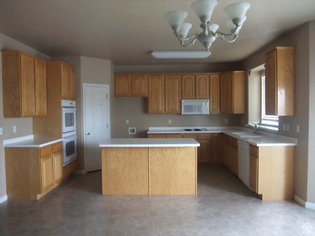 Kitchen featuring white appliances, a kitchen island, a sink, light countertops, and a chandelier