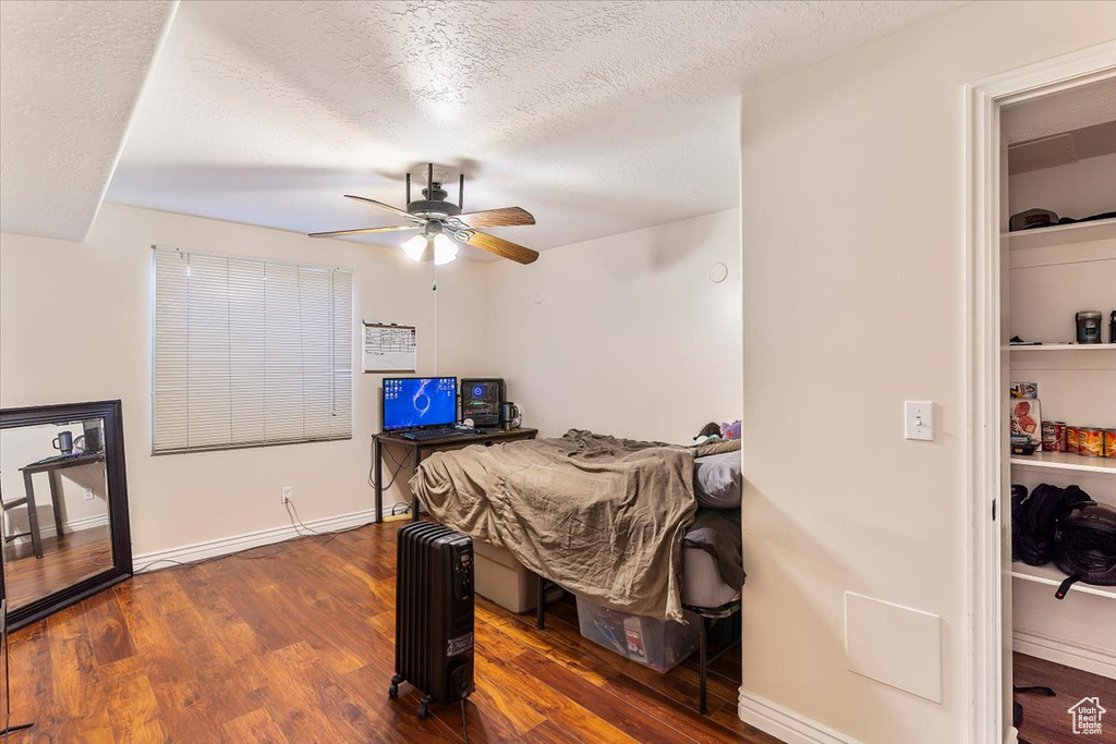 Bedroom featuring dark wood-style flooring, a textured ceiling, ceiling fan, baseboards, and radiator