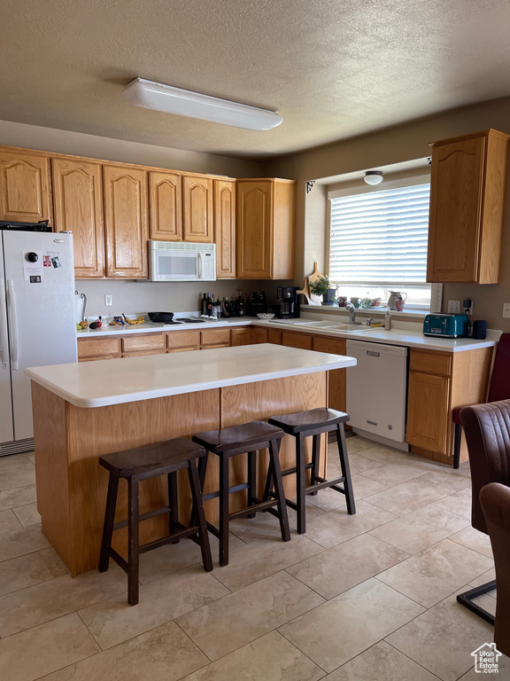 Kitchen with white appliances, a textured ceiling, a kitchen bar, light countertops, and a sink