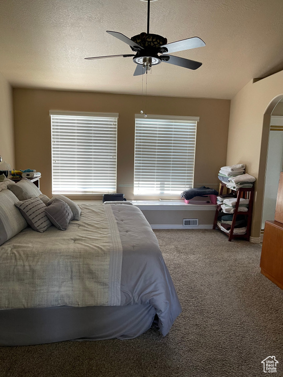 Carpeted bedroom featuring a textured ceiling, a ceiling fan, and arched walkways