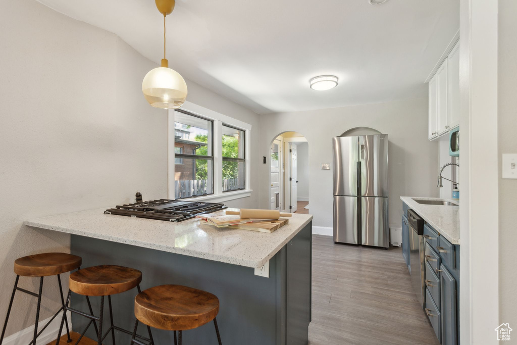 Kitchen featuring appliances with stainless steel finishes, light wood-style floors, a kitchen bar, white cabinetry, and arched walkways