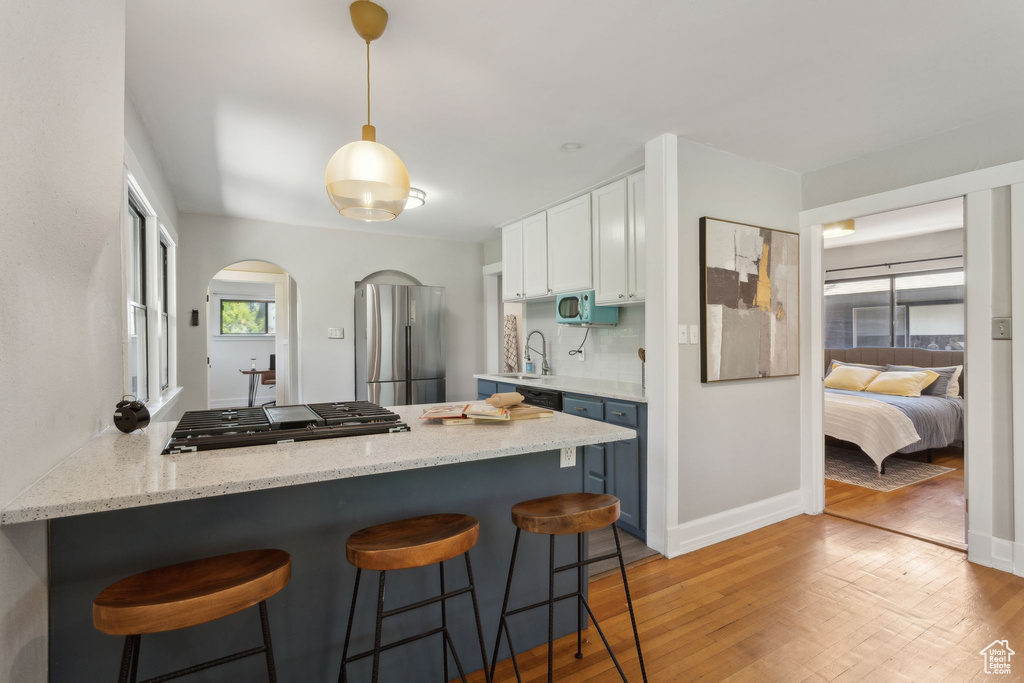 Kitchen featuring freestanding refrigerator, a sink, a peninsula, light wood finished floors, and white cabinets