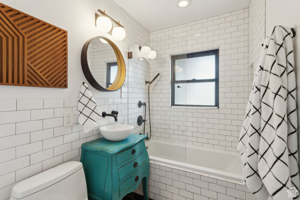 Bathroom featuring tile walls, tiled shower / bath combo, vanity, and toilet