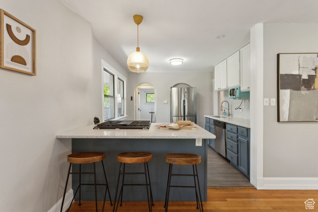 Kitchen with stainless steel appliances, a sink, a breakfast bar area, white cabinetry, and light wood-style flooring