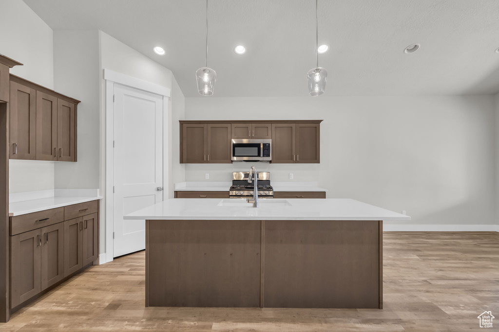 Kitchen with stainless steel microwave, a sink, light countertops, light wood-type flooring, and recessed lighting
