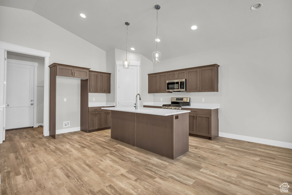 Kitchen featuring appliances with stainless steel finishes, vaulted ceiling, light countertops, light wood-style flooring, and baseboards