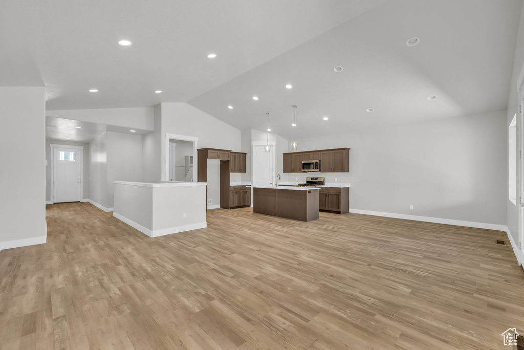 Unfurnished living room featuring lofted ceiling, light wood-style floors, a sink, baseboards, and recessed lighting