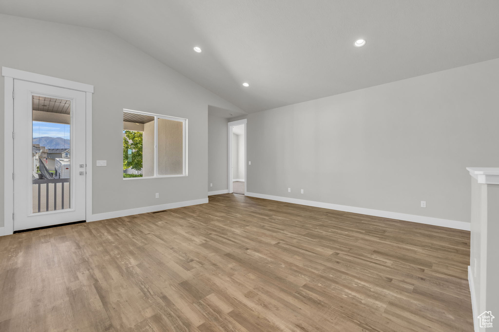 Unfurnished living room featuring lofted ceiling, light wood-style flooring, recessed lighting, and baseboards
