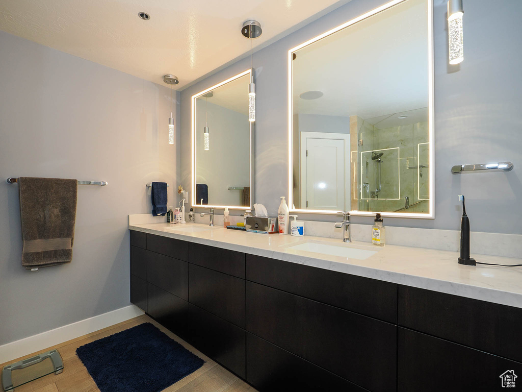 Bathroom featuring a stall shower, double vanity, baseboards, and wood finished floors