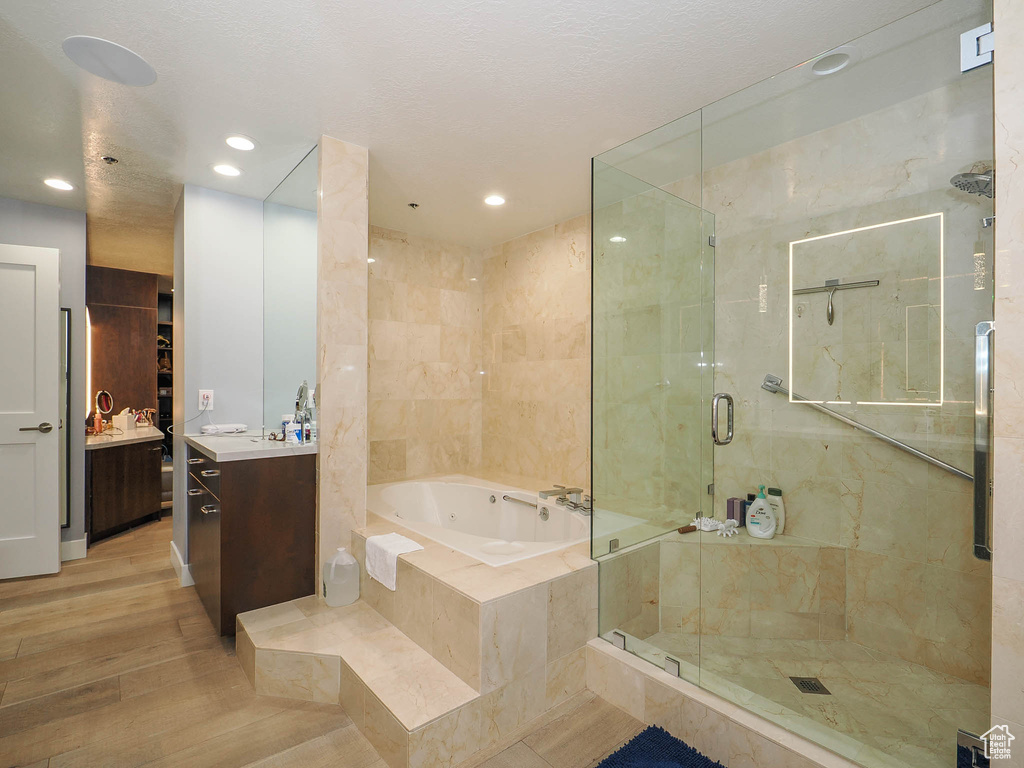 Bathroom with vanity, a tub with jets, a stall shower, wood finished floors, and recessed lighting