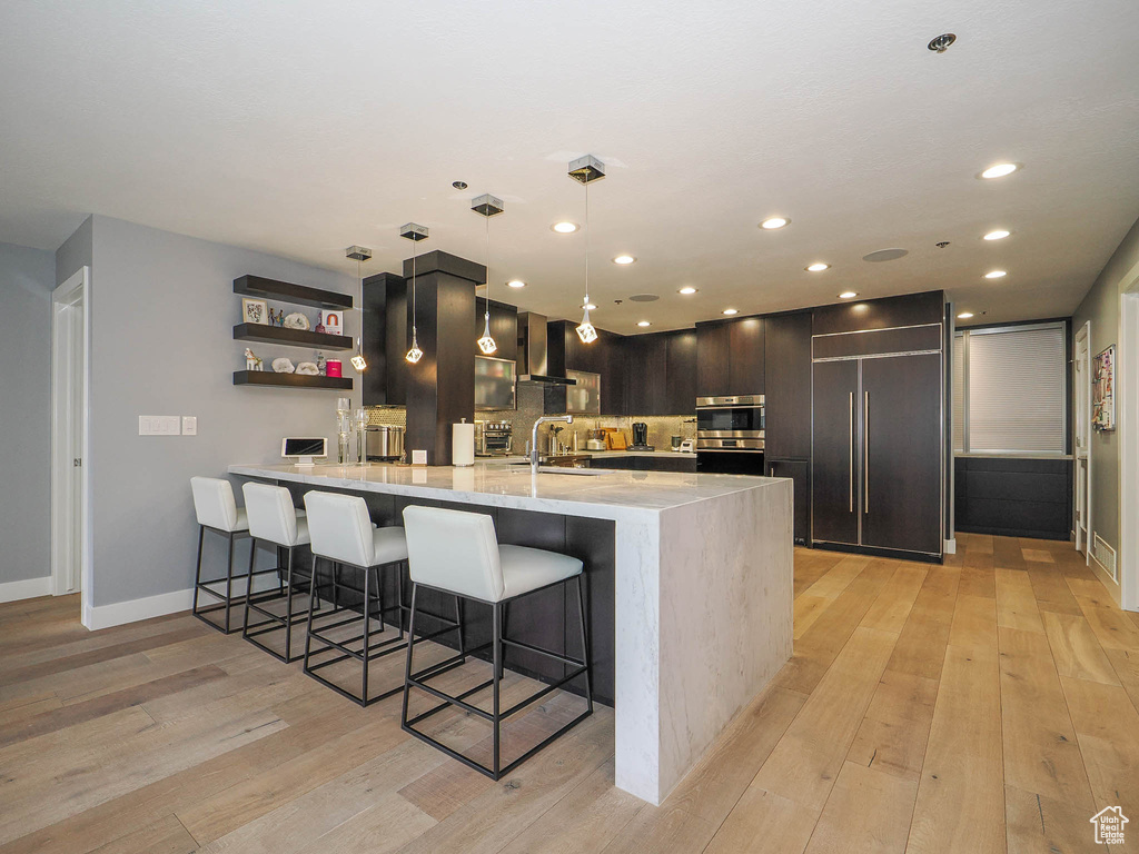 Kitchen with wall chimney exhaust hood, paneled built in refrigerator, a peninsula, a kitchen breakfast bar, and light wood finished floors