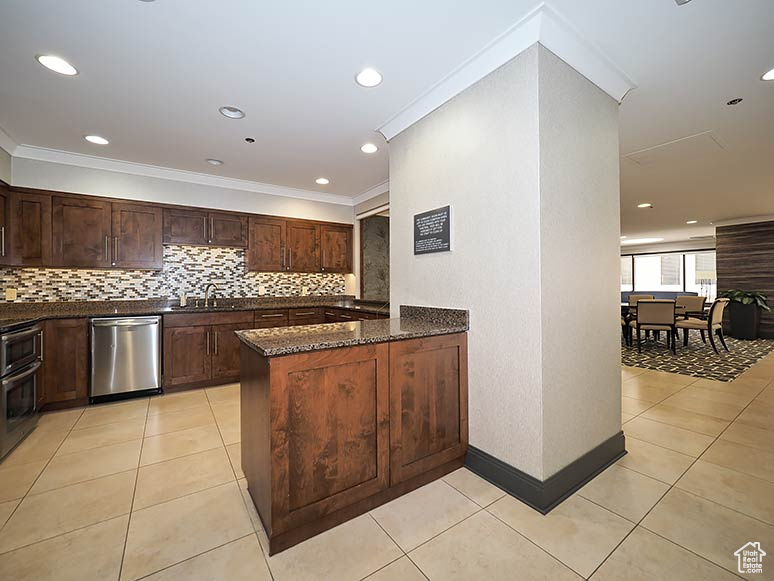 Kitchen featuring stainless steel dishwasher, backsplash, dark stone counters, a sink, and light tile patterned flooring