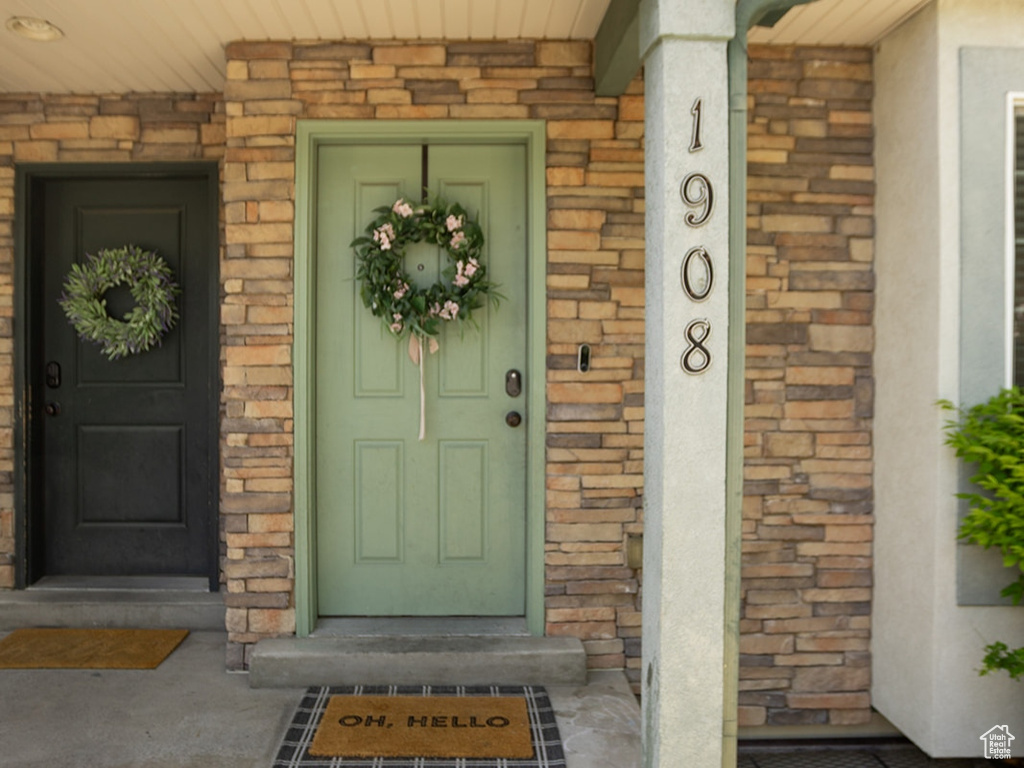 View of exterior entry with covered porch, stucco siding, and brick siding